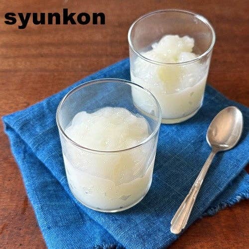 2つのグラスに入った白いデザートとスプーンが青い布の上に置かれています。