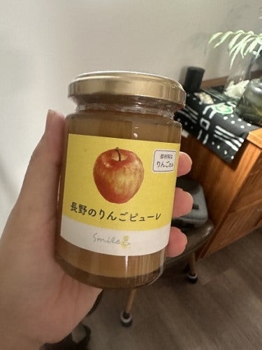 リンゴのビューレが入った瓶を手で持っている。ラベルにはリンゴのイラストと「長野のりんごピューレ」と書かれている。