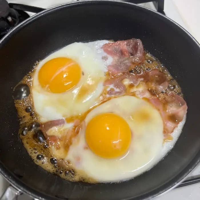 フライパンでベーコンと2つの目玉焼きが焼かれている様子。