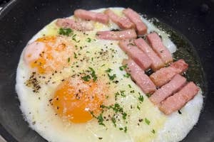 フライパンで目玉焼きとハムを調理中。刻んだハーブがかかっている。