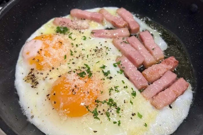 フライパンで目玉焼きとハムを調理中。刻んだハーブがかかっている。