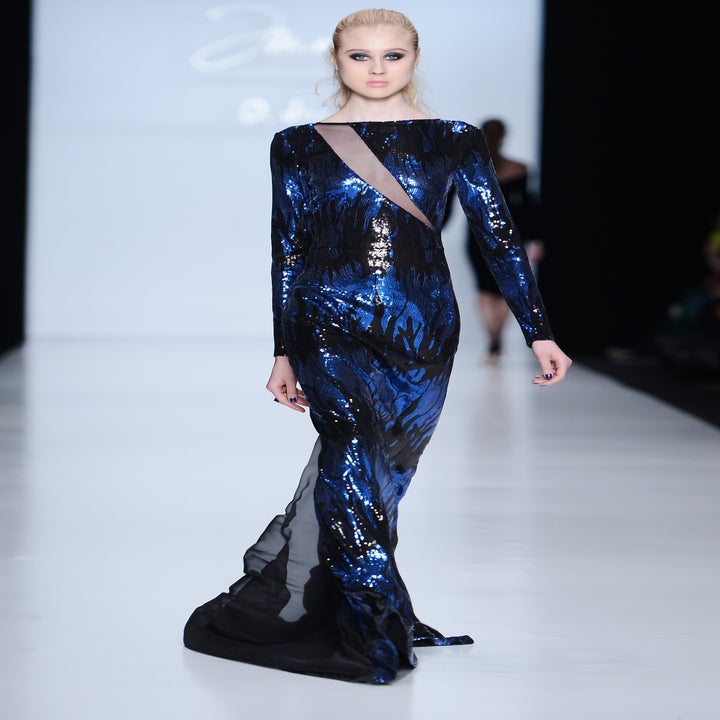 Model on runway wearing a form-fitting, long-sleeve, shimmering gown with a unique pattern and sheer sections