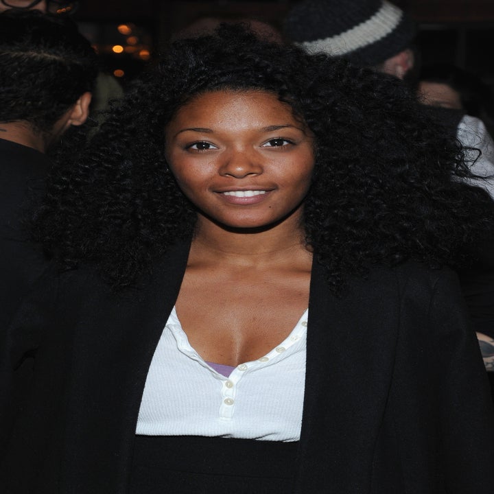 A person with a smile, wearing a white top and dark jacket, stands in a social setting