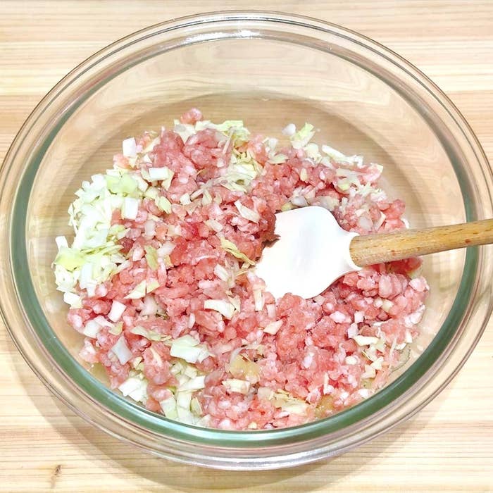 ボウルに刻んだキャベツと挽き肉を混ぜる白いスパチュラが入っている調理中の様子。