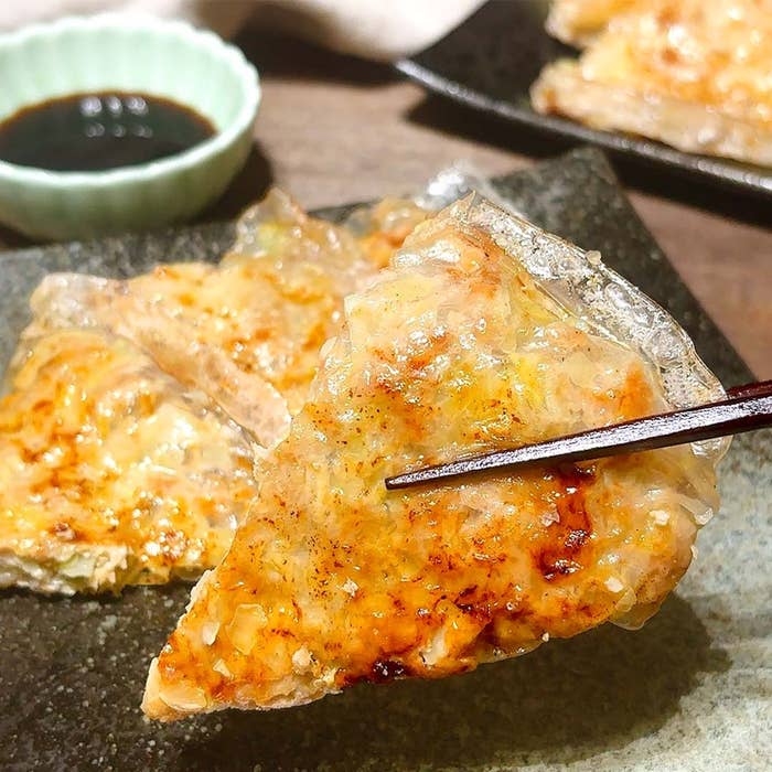 料理が箸で持ち上げられている。背景に小皿のタレが見える。