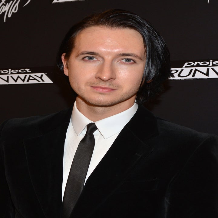Person in formal black blazer and white shirt at a Project Runway event backdrop