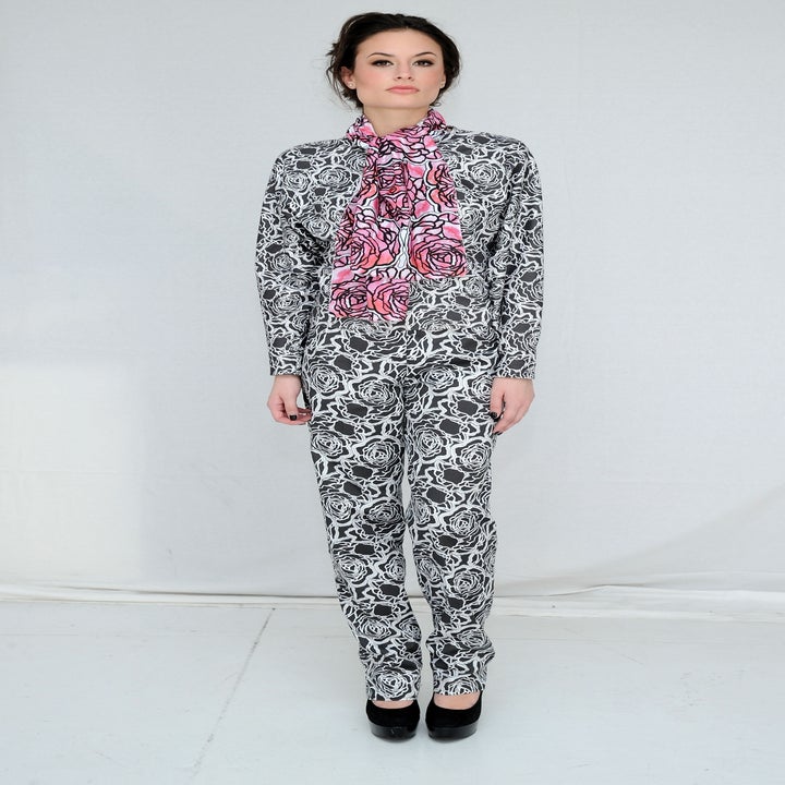 Person in matching floral-patterned outfit and scarf, standing against a plain backdrop, wearing black heels