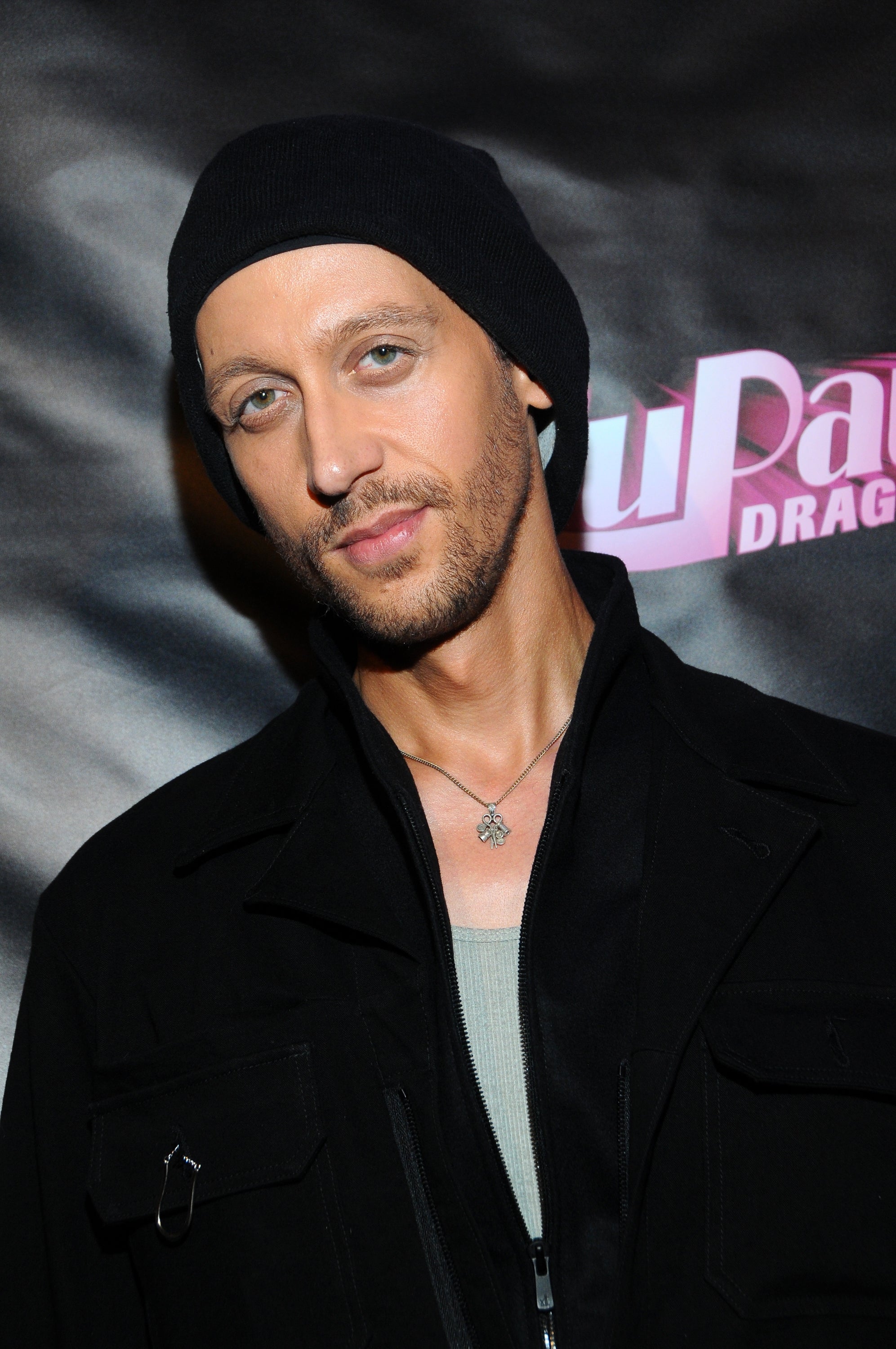 Person wearing a beanie and dark jacket at an event backdrop