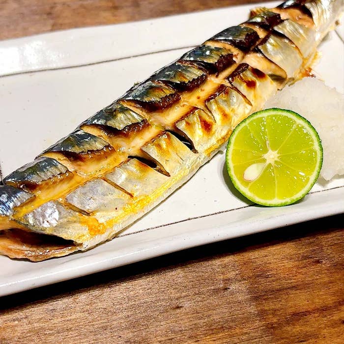 焼きサンマが白い皿に盛られており、横に輪切りの柑橘類と大根おろしが添えられています。
