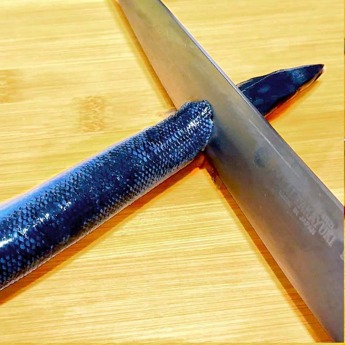 包丁で魚をまな板の上に置き、頭を切り落としている様子。