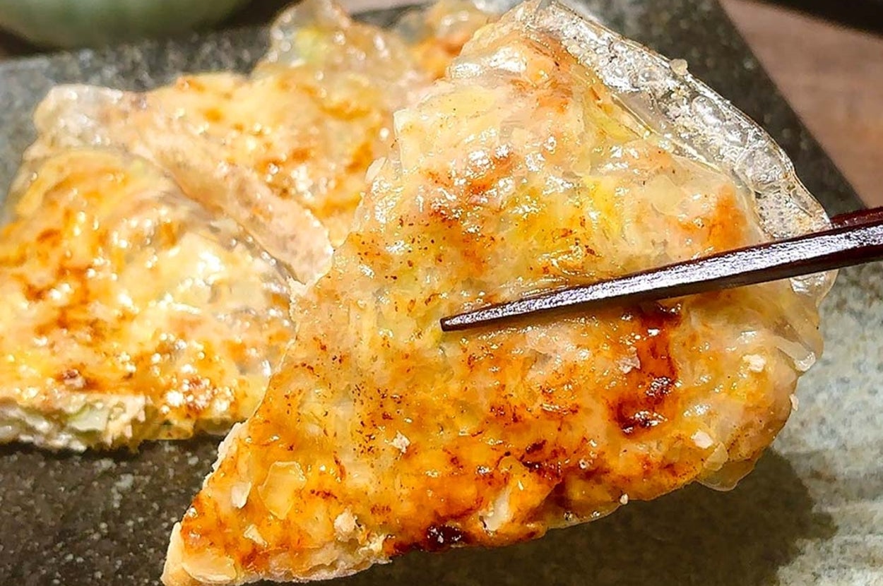餃子を箸で持ち上げた様子。パリッとした焼き目が美味しそう。背景にタレの入った小さな器が見える。