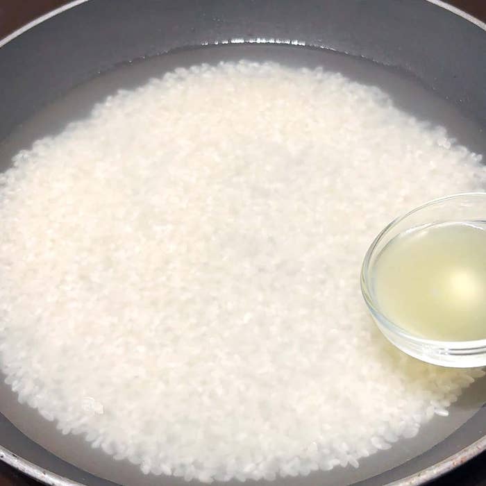 フライパンに米と水、別の小さな器に入った透明な液体がある。