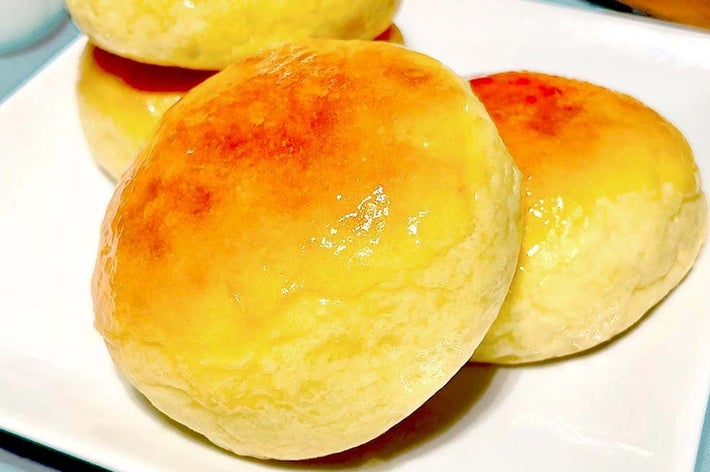 皿に乗った焼きたてのパン3個。背景にはバターとナイフが置かれた小さな木製プレートが見える。