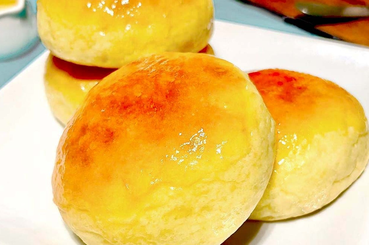 皿に乗った焼きたてのパン3個。背景にはバターとナイフが置かれた小さな木製プレートが見える。