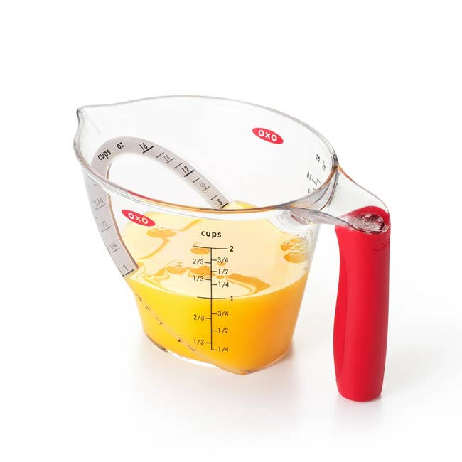 Measuring cupful  with reddish  handle, marked successful  cups and milliliters, holds liquid up   to 2/3 cup