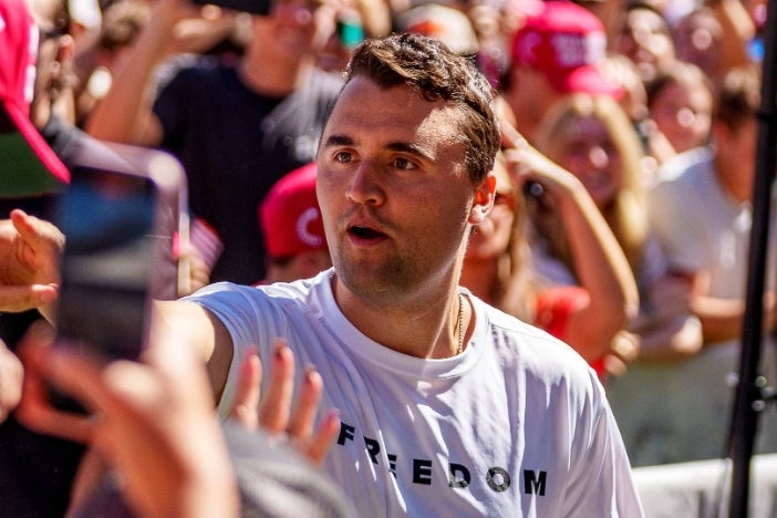 A tennis player signs autographs for fans at an outdoor event, wearing a T-shirt with the word "FREEDOM." The crowd holds out items for him to sign