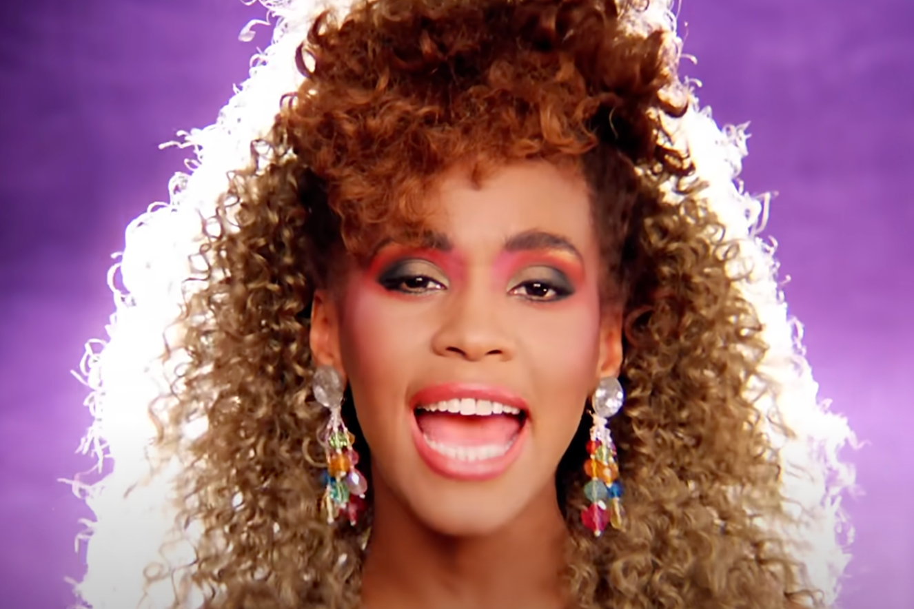 Person singing passionately, with curly hair and statement earrings, against a vibrant background