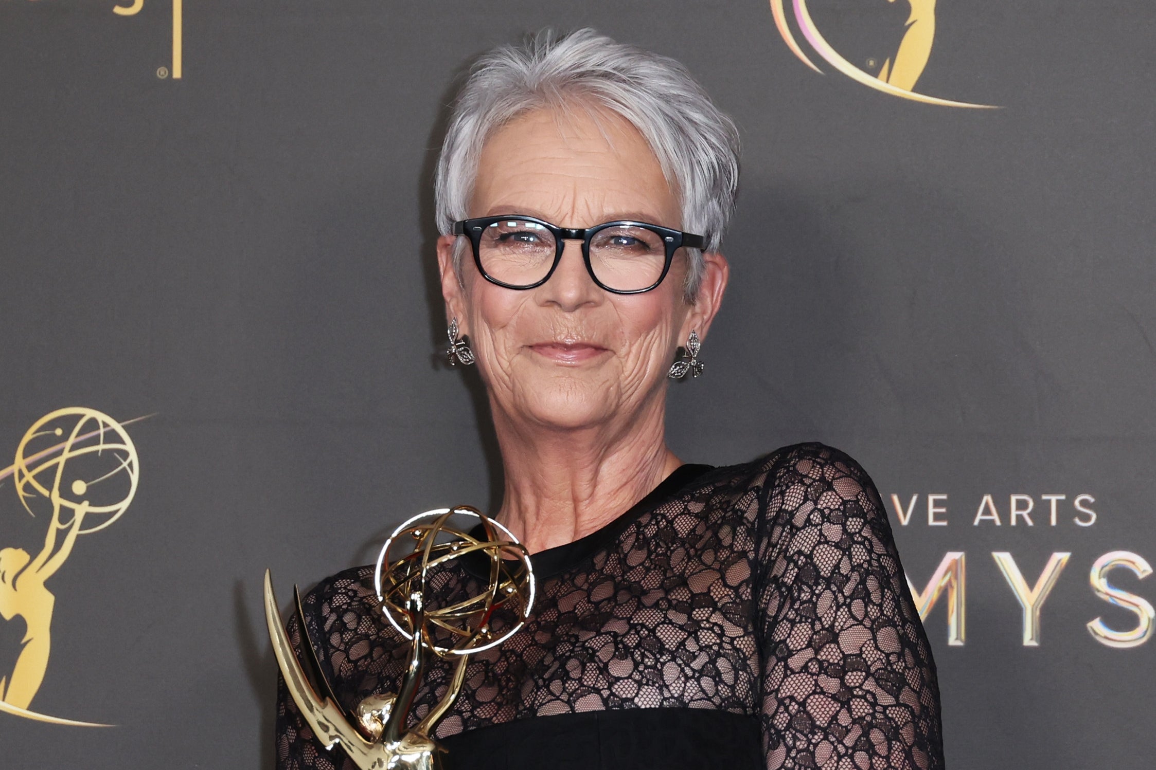 Jamie Lee Curtis in a lace dress holding an Emmy