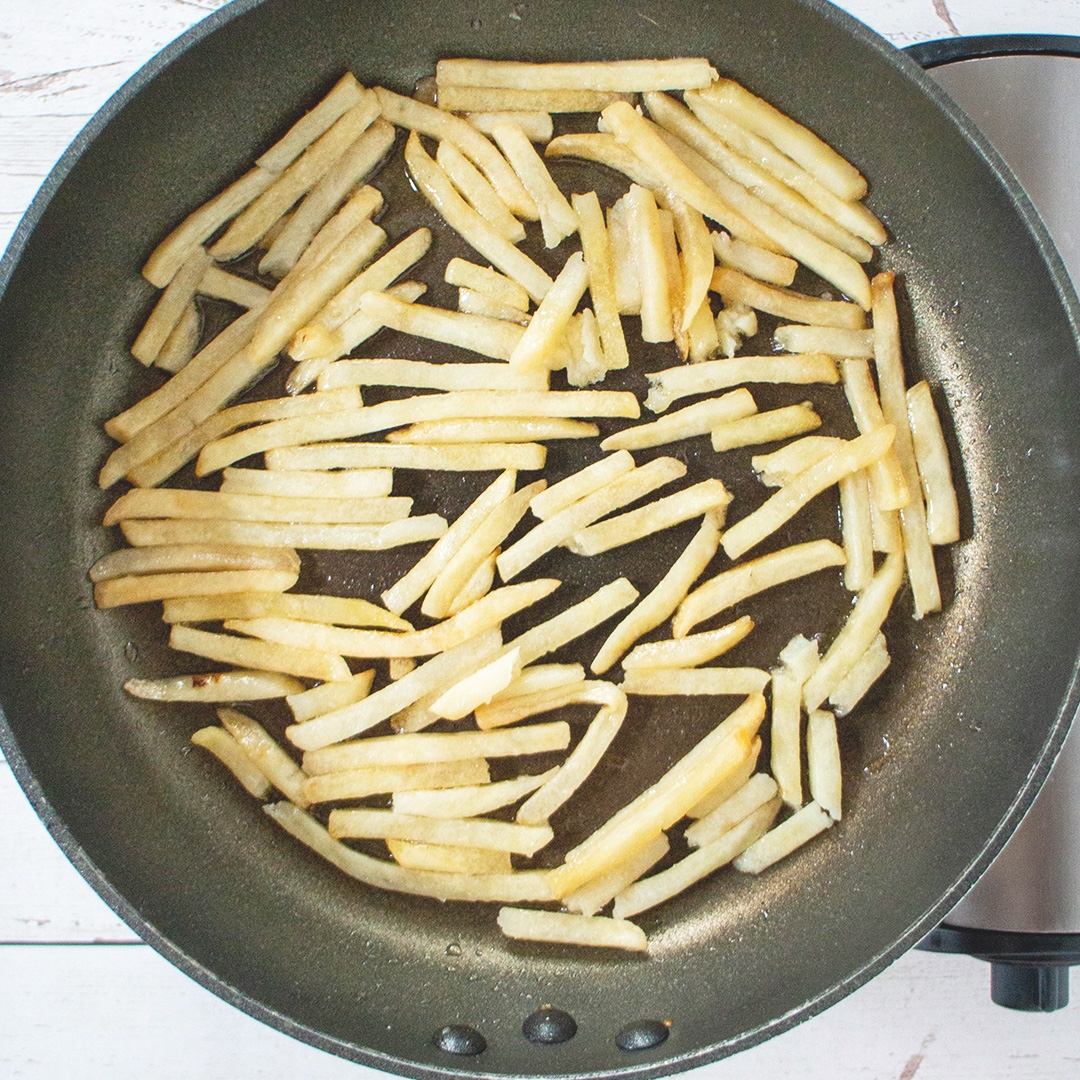 フライパンに並べられた細長いフライドポテトが調理されている様子。