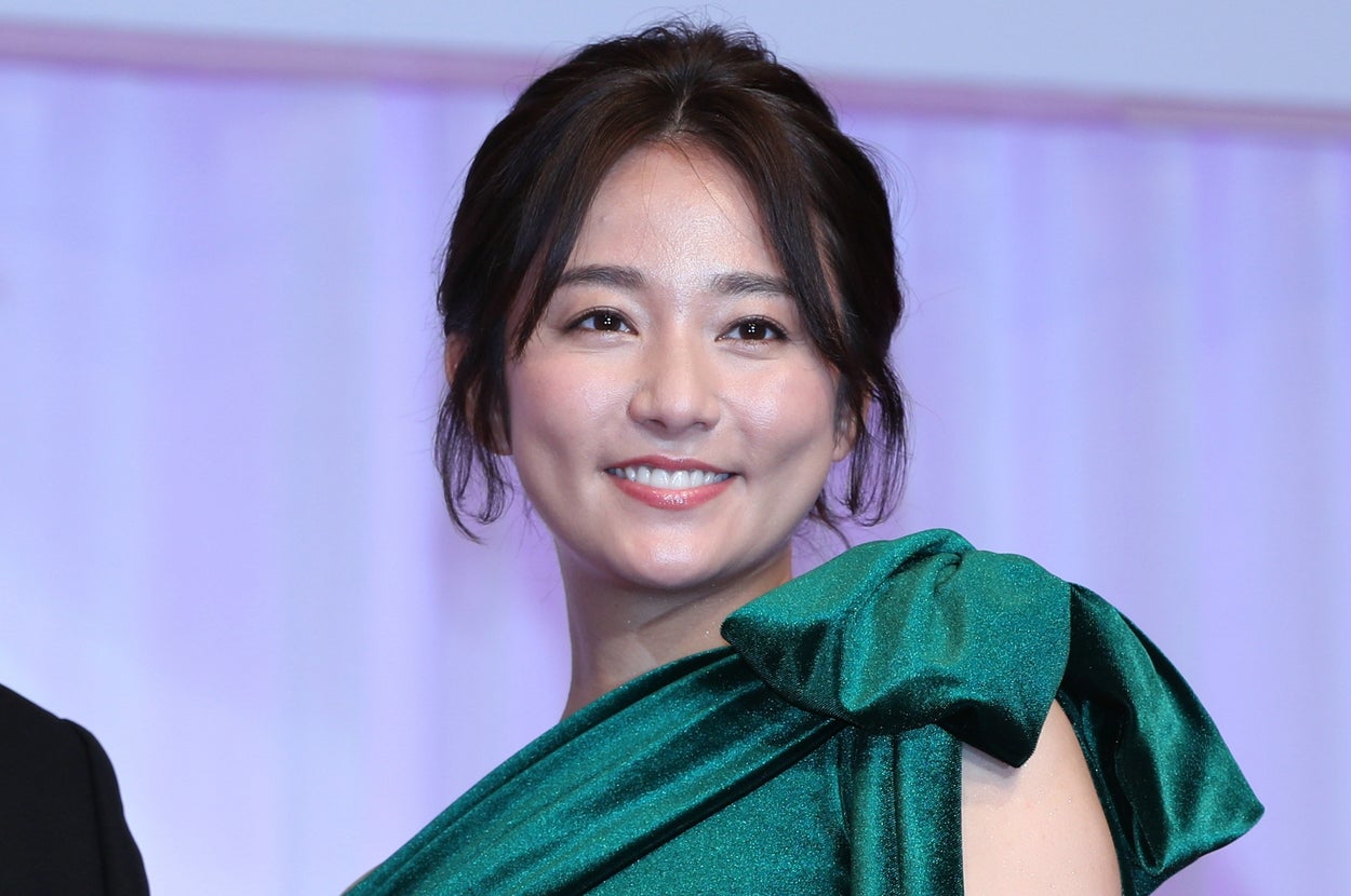 有名人が豪華なドレスを着て、トロフィーを手に微笑んでいるシーン。
