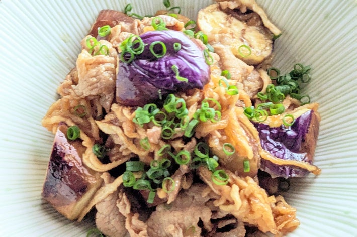 茄子と豚肉の炒め物、刻みネギをトッピング、白いボウルに盛り付けた料理。