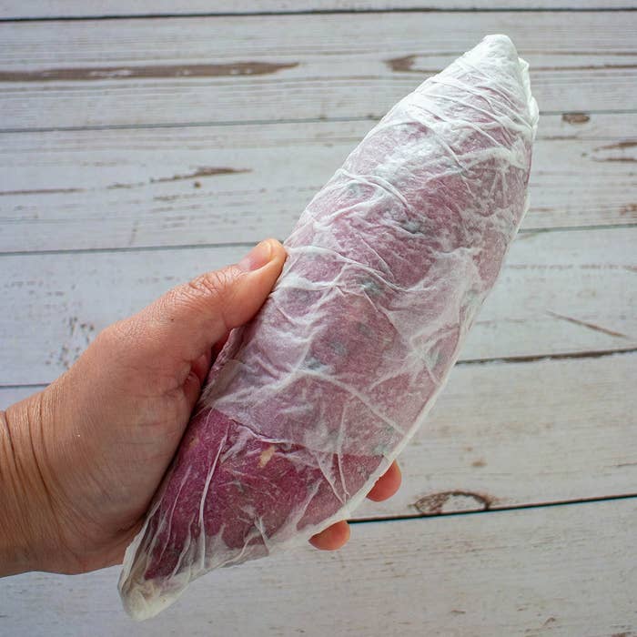 手に持たれたラップされた肉の塊が木製のテーブルの上に置かれている。