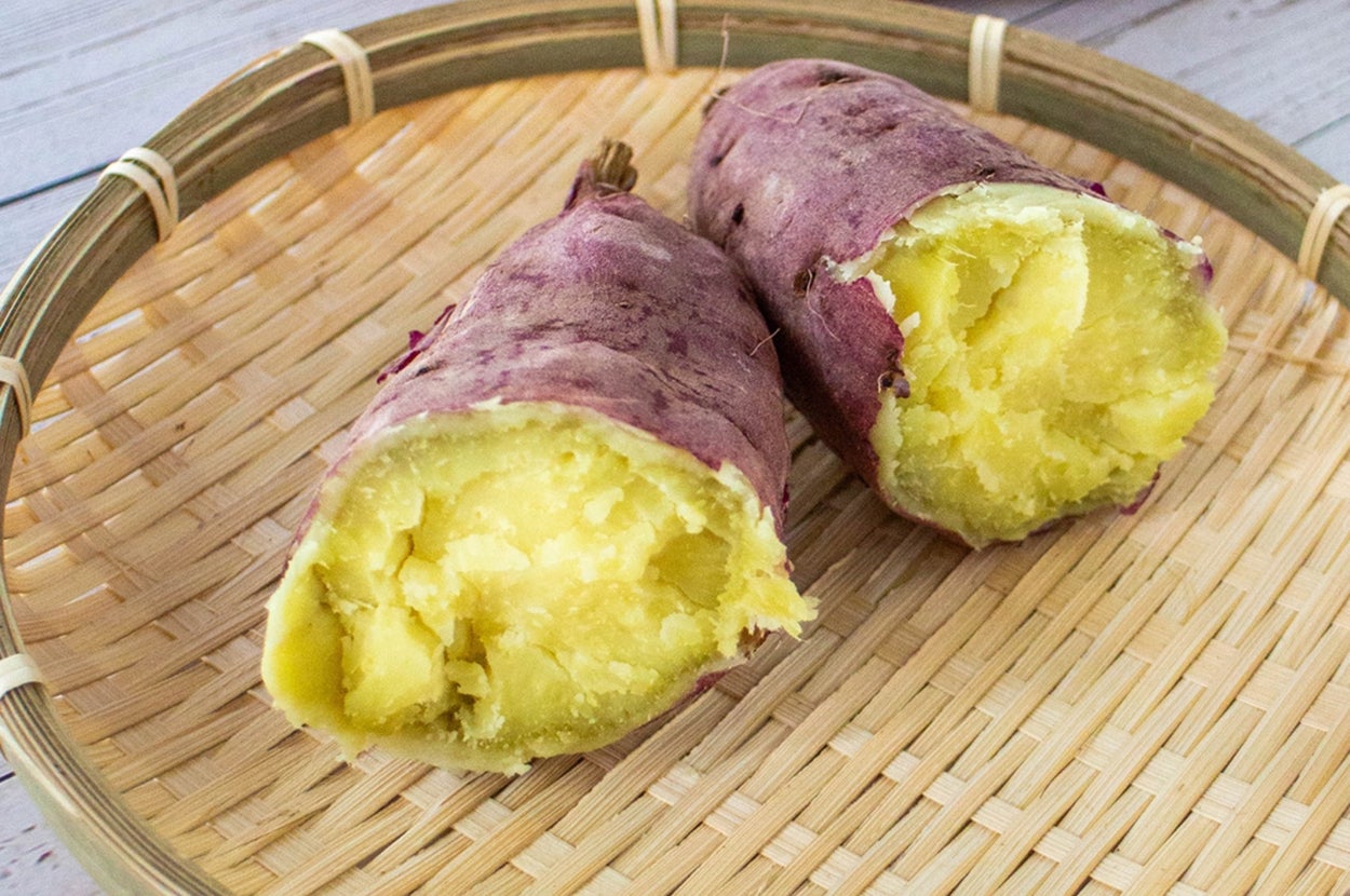 竹ざるに盛った焼き芋が半分に切られ、柔らかく焼き上がっている。奥に未調理のサツマイモも見える。