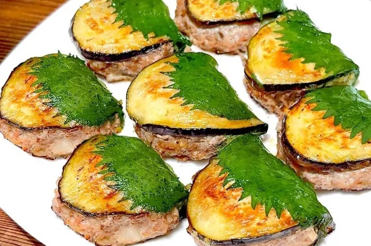 大葉と茄子で挟まれたハンバーグ風料理が白い皿に盛られている。