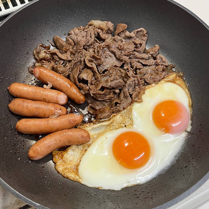 フライパンで調理されたソーセージ、目玉焼き、焼き肉が見える朝食料理。