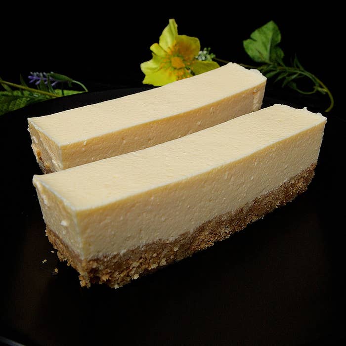 2切れのチーズケーキが黒い背景に置かれており、上には飾りの花がある。
