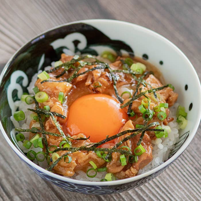 ご飯の上に生卵、細切り海苔、ネギ、鶏肉が載った丼料理の画像です。