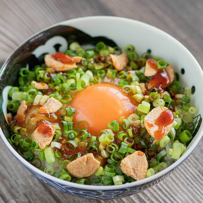 ネギ、卵黄、ソース、ガーリックチップを乗せたご飯のボウル。食欲をそそる美味しそうな料理です。
