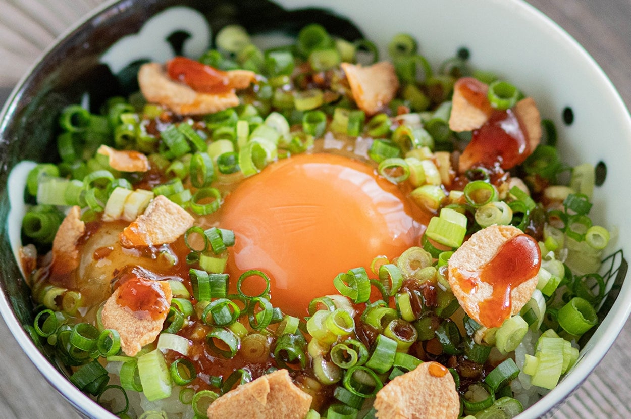 器に盛られたうどんの上に卵、ネギ、揚げ玉、タレがトッピングされている。