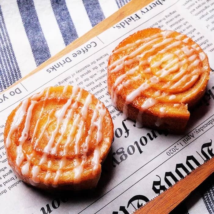 新聞紙の上に置かれたアイシングがかかった2つのシナモンロール。