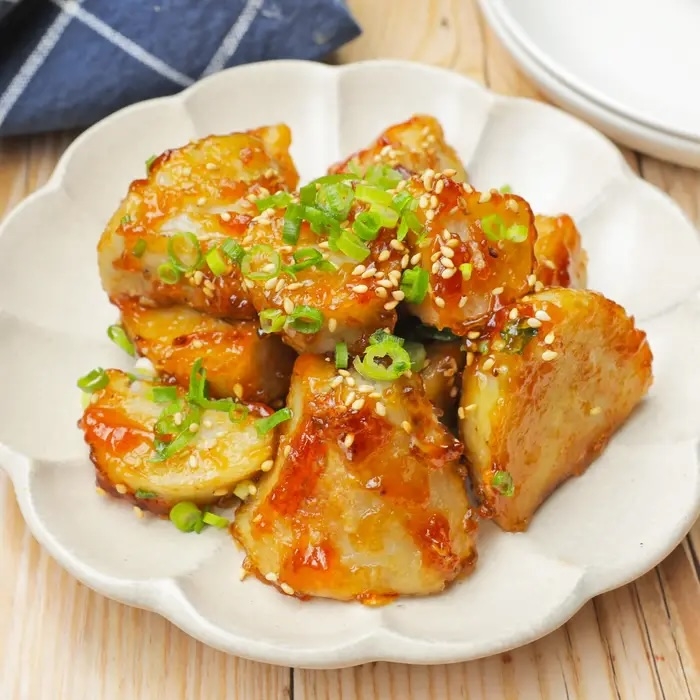 白い皿に盛られた、ごまやネギで飾られた美味しそうな照り焼き風の料理。