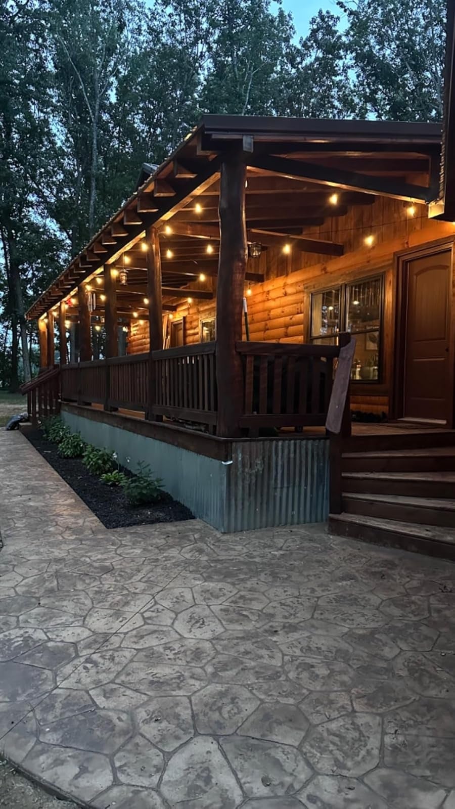 Wooden compartment  with a ample  structure  illuminated by drawstring  lights, surrounded by trees. Stone pathway leads to steps. Cozy, rustic ambiance  astatine  dusk