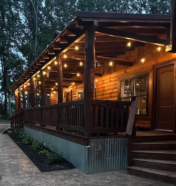 Wooden compartment with a ample structure illuminated by drawstring lights, surrounded by trees. Stone pathway leads to steps. Cozy, rustic ambiance astatine dusk