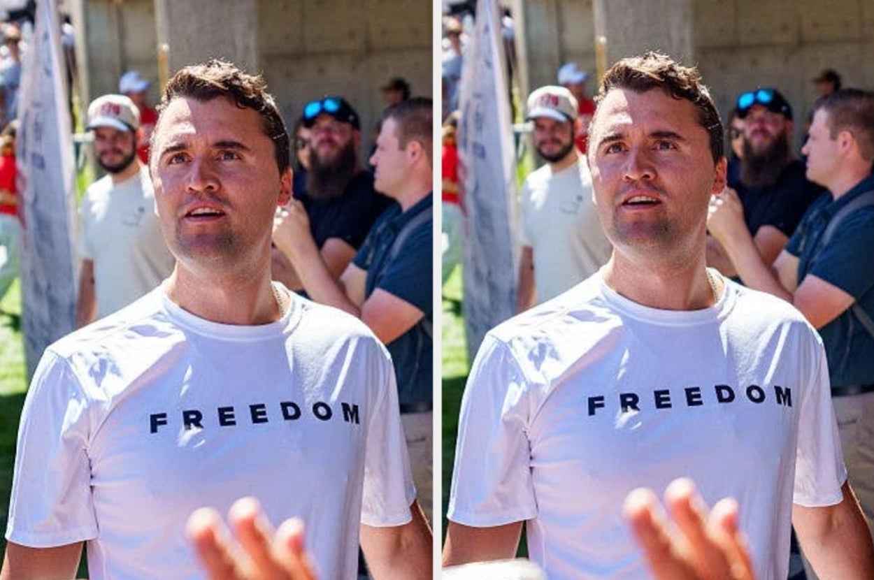Charlie Kirk wearing a T-shirt with "FREEDOM" text stands outdoors, engaged in conversation with a group in the background