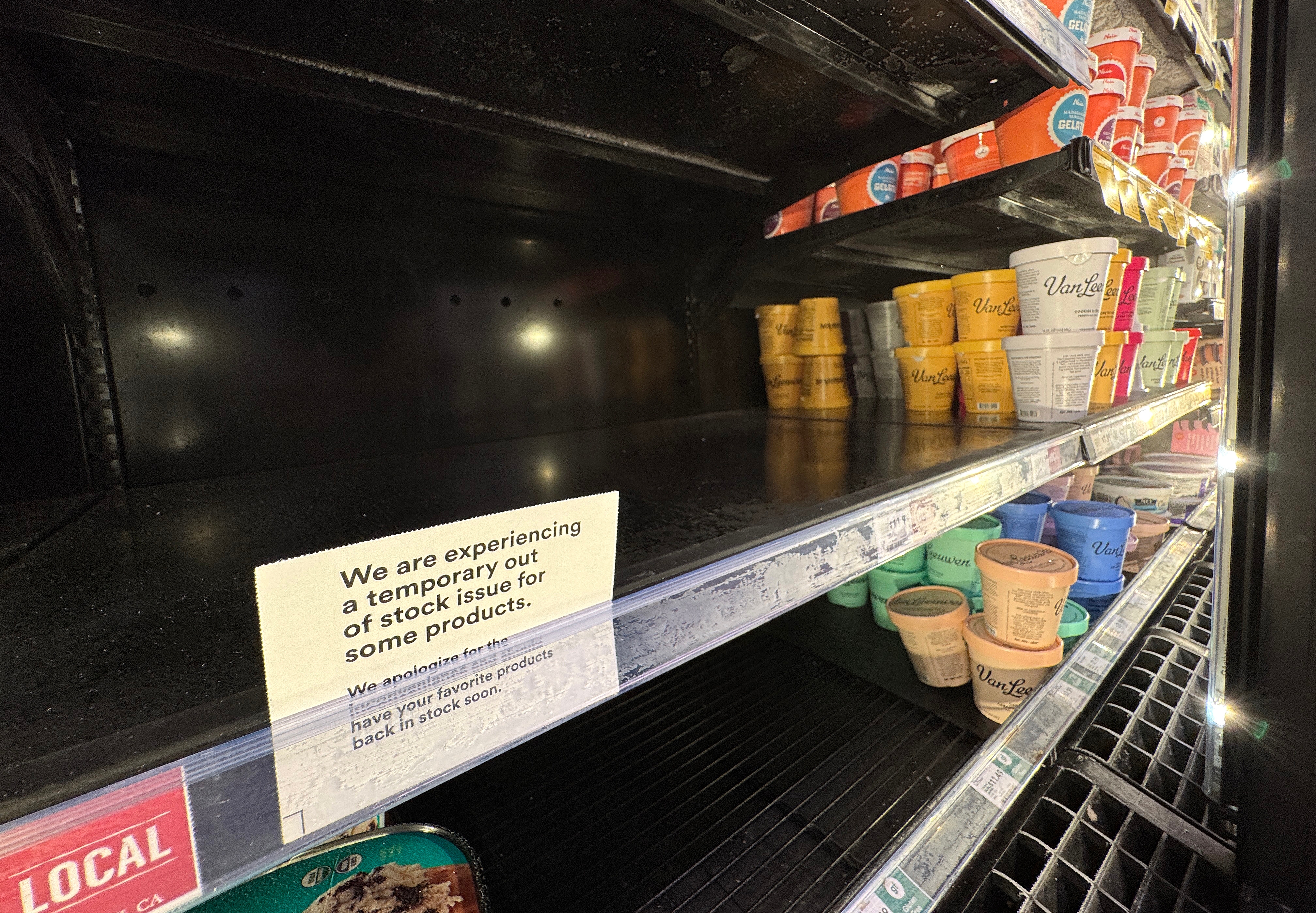 Store freezer with mostly empty shelves and a note about a temporary out-of-stock issue for some products. A few ice cream tubs remain
