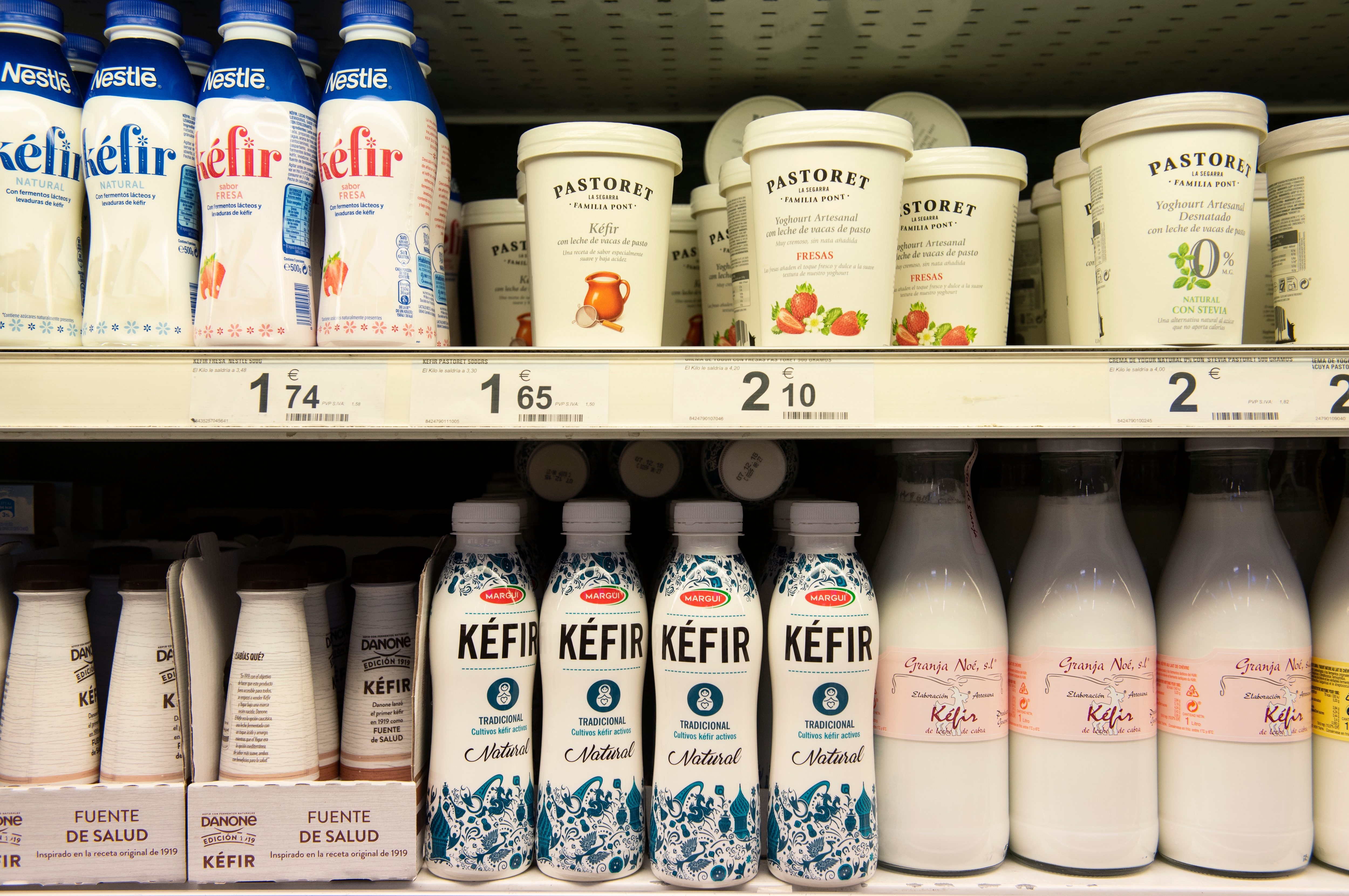 Dairy aisle with various kefir products, including bottles and containers from different brands, displayed on shelves with visible price labels