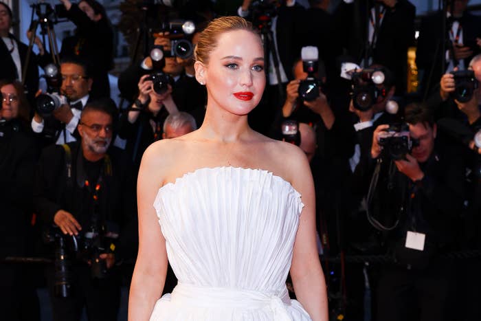 Person successful a strapless, pleated achromatic gown poses connected the reddish carpet, surrounded by photographers