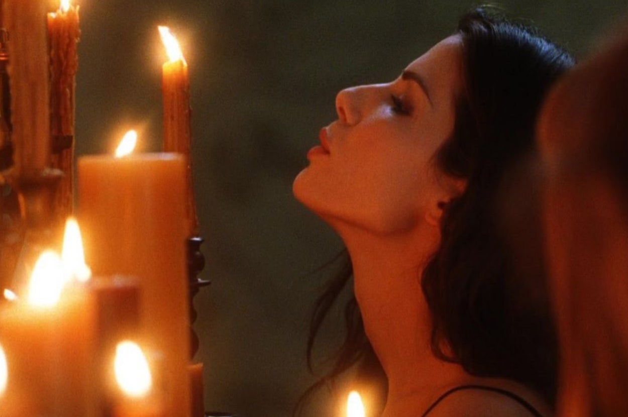 A woman with long, dark hair is tilting her head back, surrounded by lit candles, creating an introspective and serene atmosphere