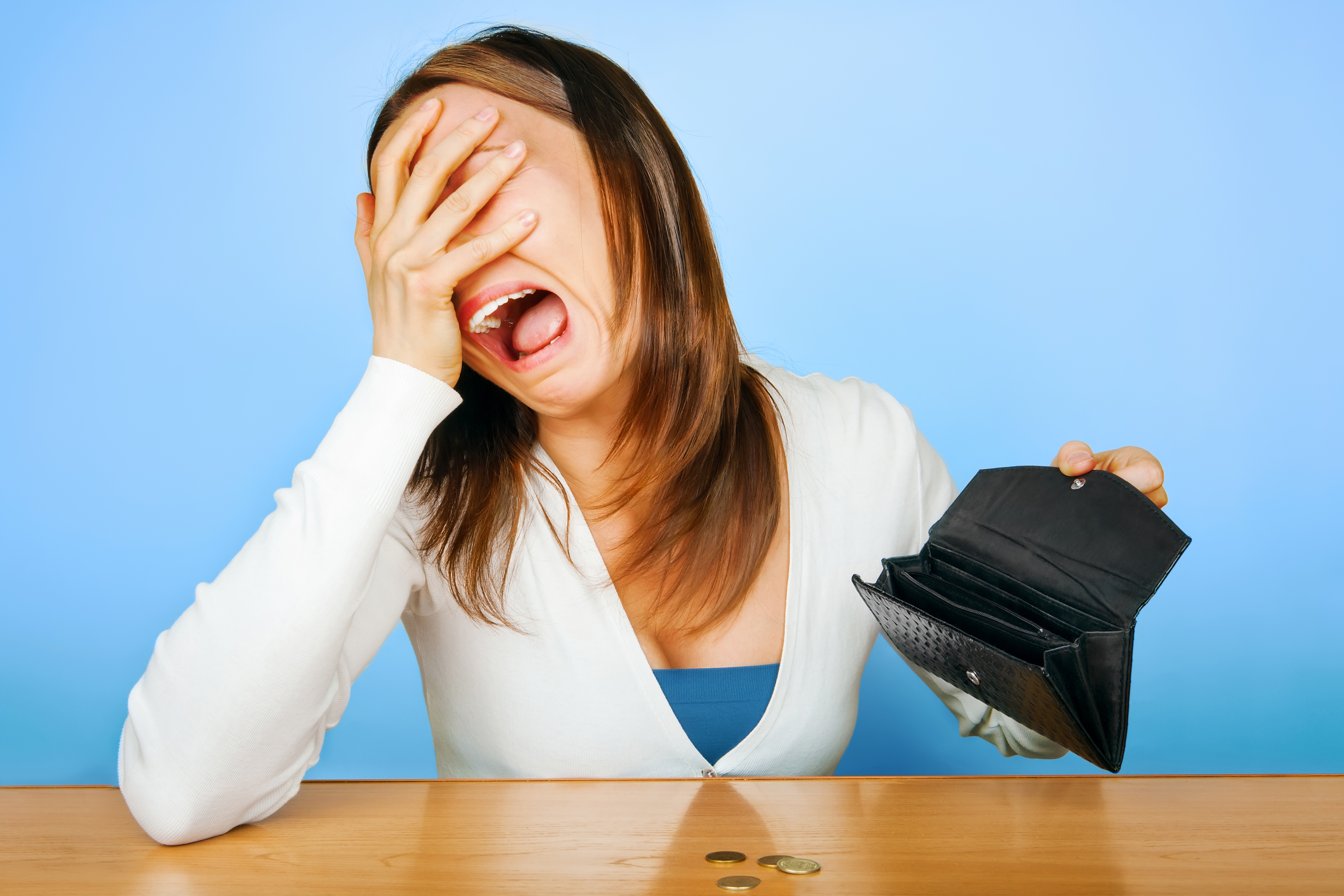 Person in distress with hand on face and open, empty wallet on table