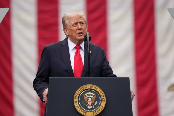 Person astatine podium with U.S. seal, speaking successful beforehand of striped backdrop. Formal attire with a tie