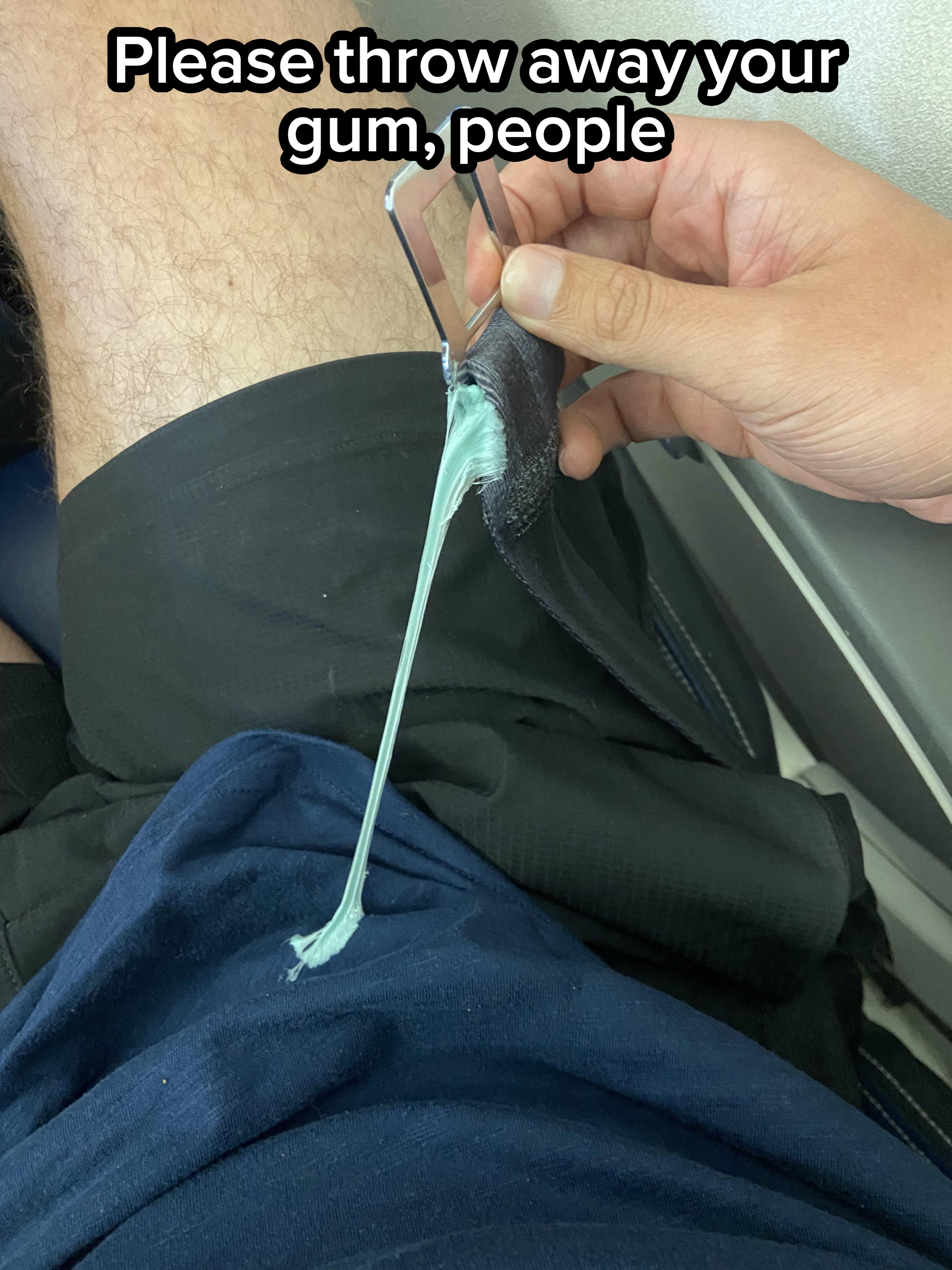 Person removing a piece of gum stuck to black shorts using a metal object, seated