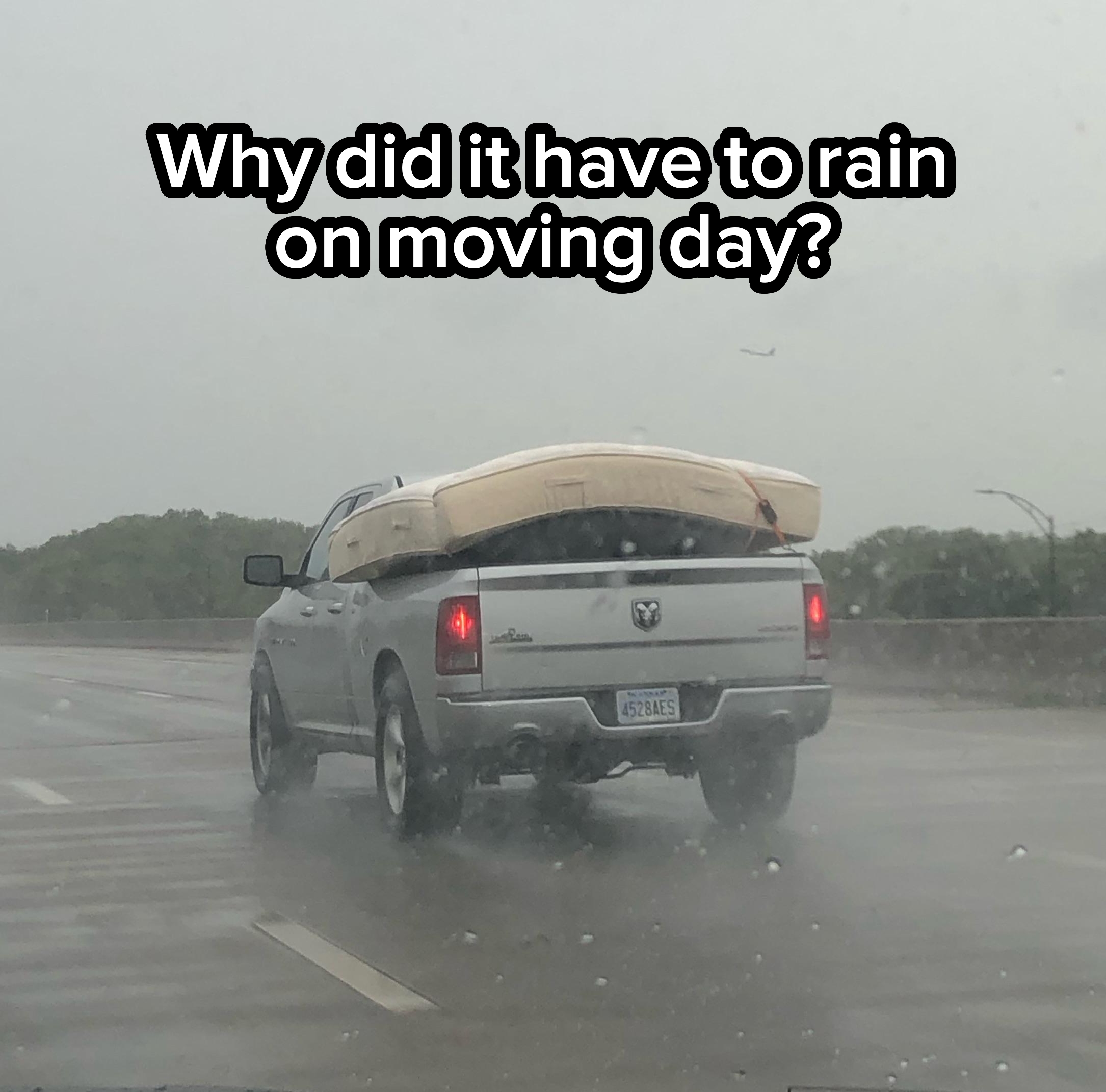 A pickup truck drives on a rainy highway with a mattress precariously balanced on its roof