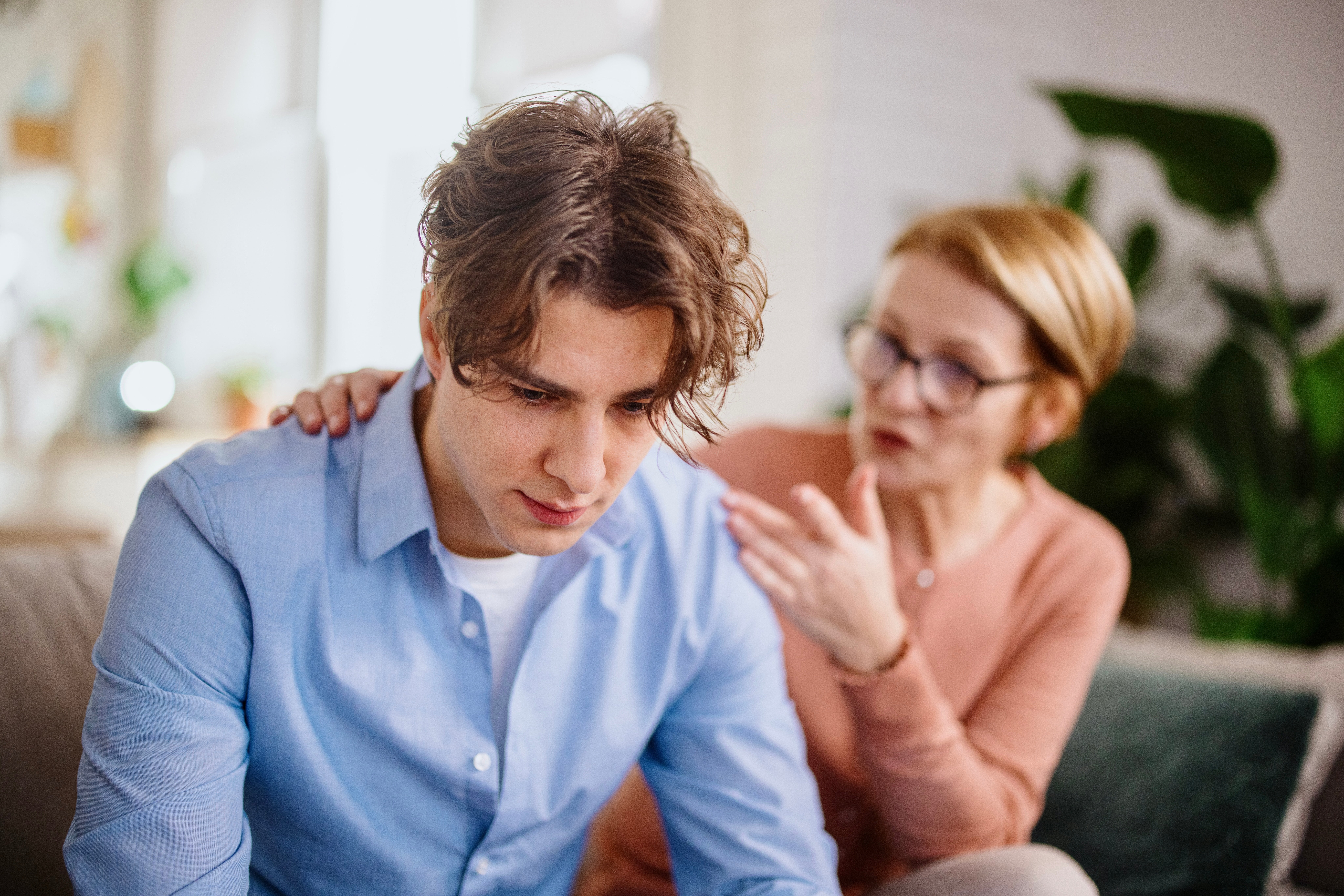 En bekymret person trøster noen som sitter på en sofa; De ser ut til å være engasjert i en støttende samtale