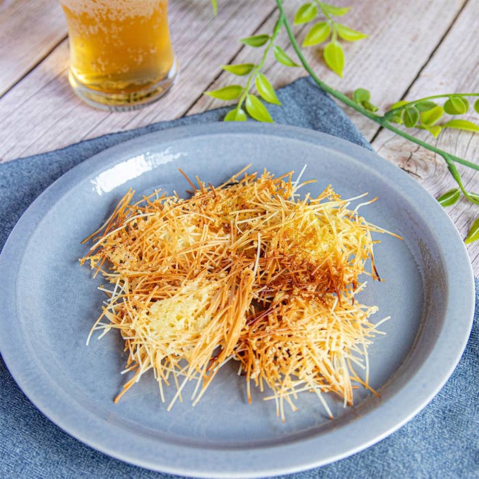 プレートにのせた揚げたそうめんのパリパリおつまみ。背景にビールと植物。
