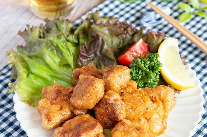 お皿に盛られた納豆揚げがレタス、レモン、パセリとトマトで飾られています。後ろにビールのグラスが見える。