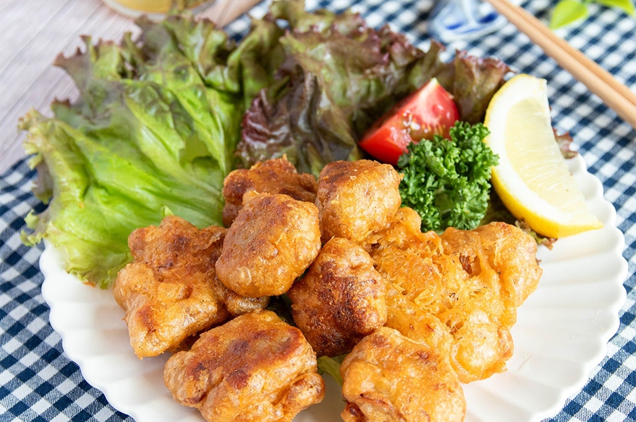 お皿に盛られた納豆揚げがレタス、レモン、パセリとトマトで飾られています。後ろにビールのグラスが見える。